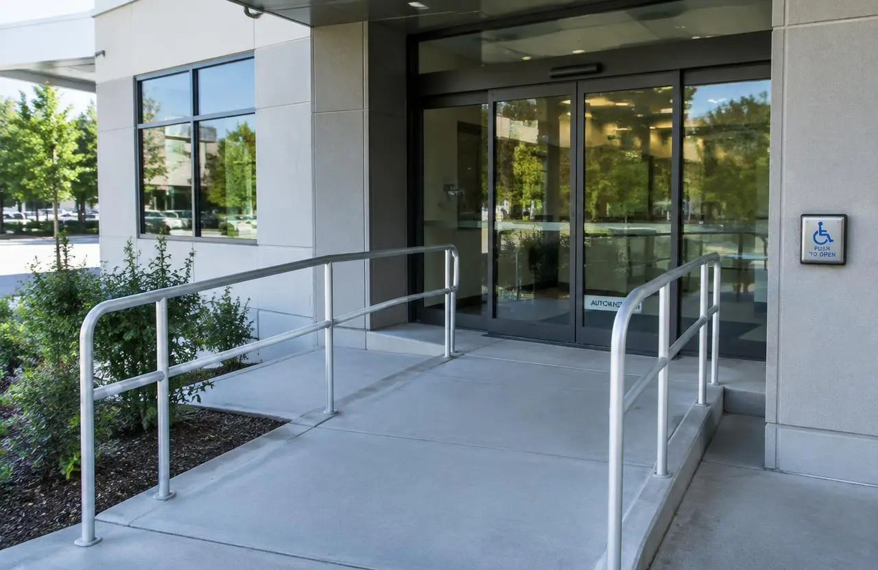 Illustrative accessible entrance with ramp, handrails and a door operator button